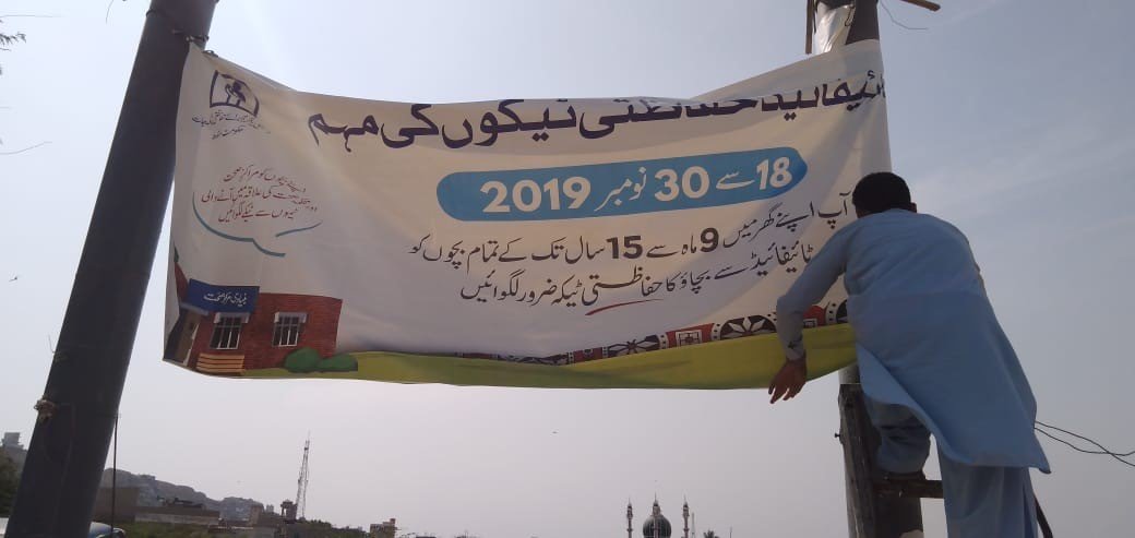 Photo: Hanging up a banner advertising a typhoid conjugate vaccine campaign in Pakistan in 2019. Credit: TyVAC/PHC Global